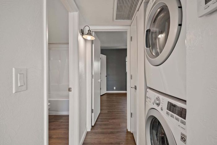 Modern apartment hallway featuring a sleek stacked washer-dryer unit beside a spacious bathroom and inviting hardwood floors.