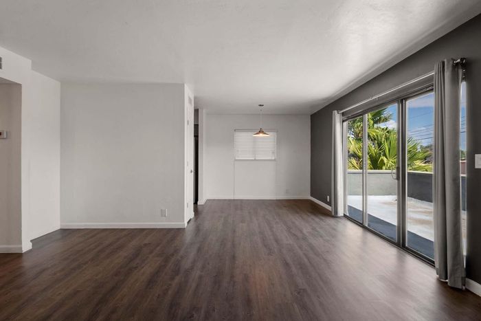 Bright and spacious living area with sleek wood flooring, large sliding glass doors opening to a balcony, and a contemporary pendant light for a modern touch.