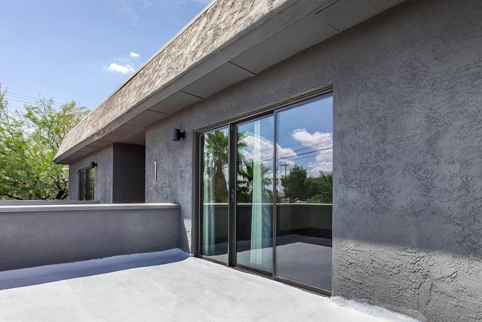 Modern apartment exterior featuring a spacious balcony with expansive glass sliding doors, surrounded by lush greenery and a clear blue sky.