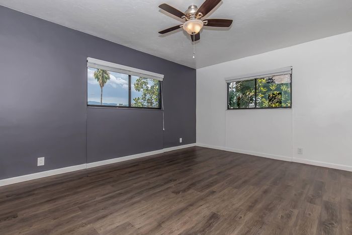 Bright and inviting room with chic dark hardwood floors and large windows offering scenic palm tree views, complete with a stylish ceiling fan for comfort.