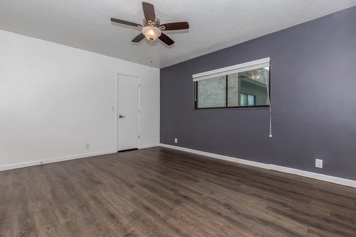 Modern bedroom with elegant wood flooring, a sleek ceiling fan, and a large window allowing natural light.