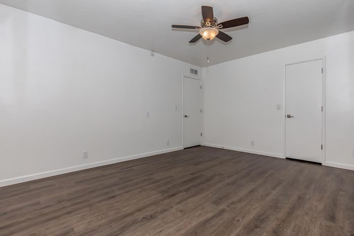 Sleek, modern room with pristine white walls and elegant dark wood flooring, complemented by a stylish ceiling fan.