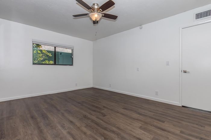 Bright, spacious room with sleek wooden floors, a modern ceiling fan, and a large window offering a tranquil view.