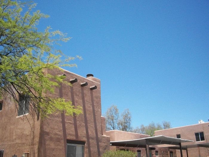 Charming adobe-style apartment with rustic accents and clear blue sky backdrop, perfect for serene living in a picturesque setting.