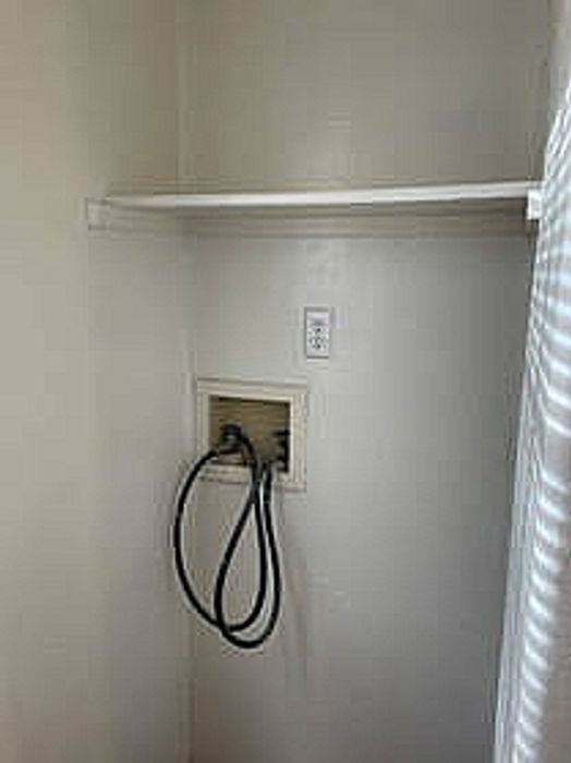 Compact laundry area with utility connections and an overhead shelf, perfect for efficient use of space.