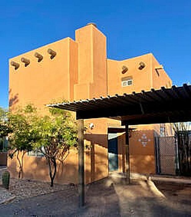 Charming adobe-style home with modern design, bathed in warm sunlight, featuring a unique architectural facade and carport.