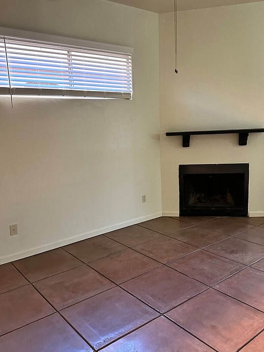 Cozy living room featuring elegant terracotta floor tiles, a stylish fireplace, and abundant natural light through sleek blinds.