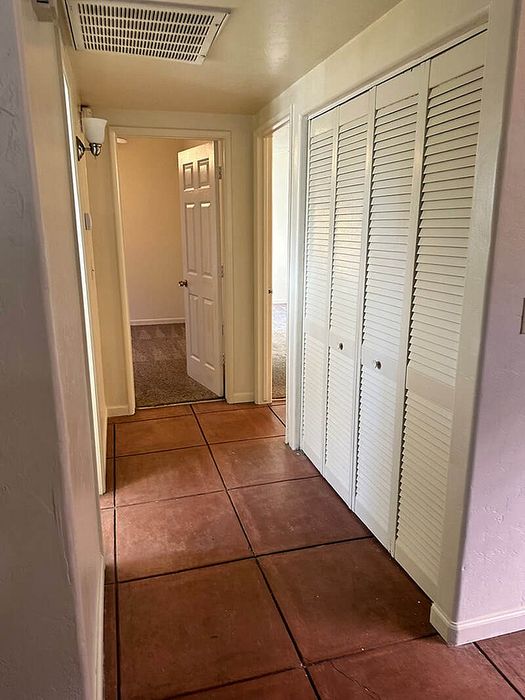 Inviting hallway with warm terracotta floor tiles, leading to cozy carpeted rooms, perfect for a welcoming home atmosphere.
