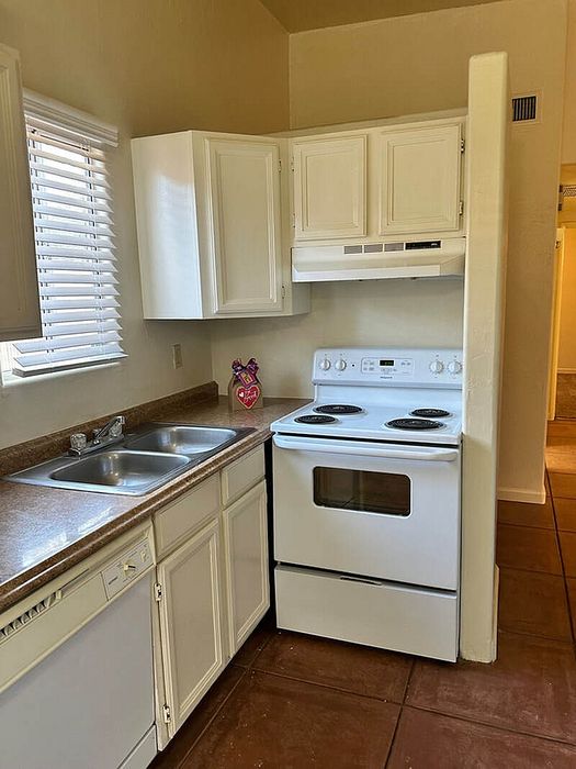 Charming kitchen with natural light, featuring white cabinetry, modern appliances, and a dual sink.