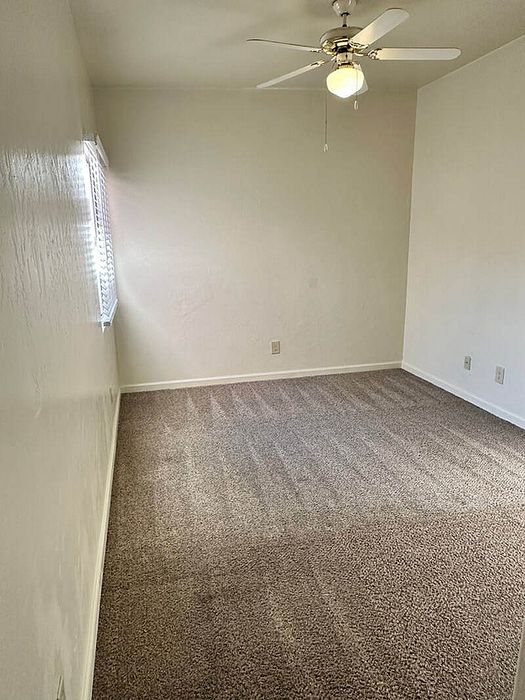 Bright, newly carpeted room with ceiling fan and window blinds, ideal for a cozy bedroom setup.