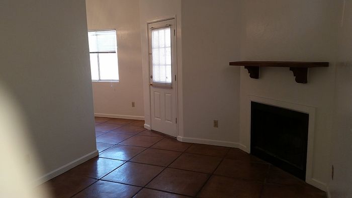 Inviting living area with rustic tile flooring, natural light from a large window, and a cozy fireplace nook.