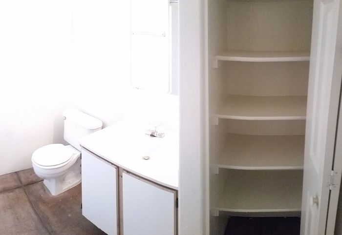 Bright bathroom featuring a modern vanity, efficient toilet, and spacious built-in shelving for ample storage.
