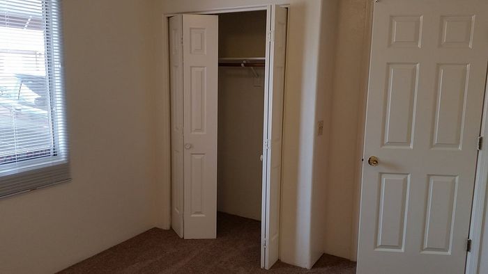 Bright interior featuring a cozy closet with double doors, plush carpet, and ample natural light through large window blinds.