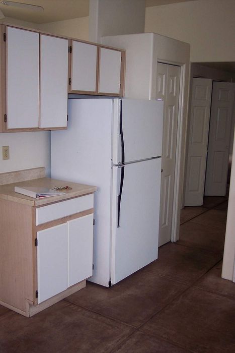 Charming kitchen corner featuring sleek white cabinets and a spacious refrigerator, leading into a cozy hallway with ample storage.