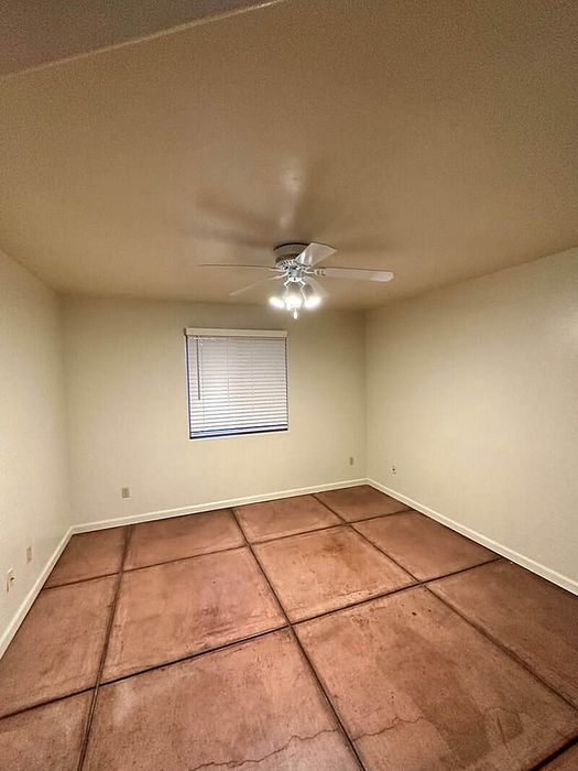 Bright, spacious bedroom with warm-toned tiled flooring, ceiling fan, and natural light from a window with blinds.