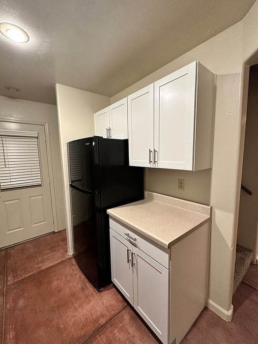 Charming kitchen corner with sleek black refrigerator, modern white cabinets, and cozy lighting.