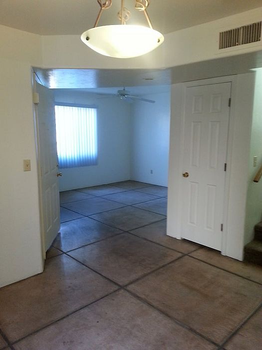 Inviting apartment interior showcasing a bright, open room with tiled flooring, white walls, and ample natural light from a large window, perfect for a cozy living area.