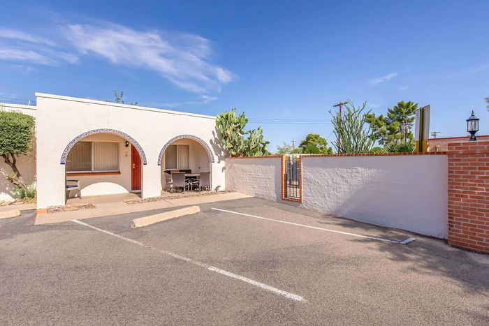 Charming southwestern-style property with elegant arches, inviting outdoor seating, and vibrant desert landscaping under a clear blue sky.