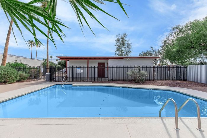 Inviting outdoor pool area with clear blue water, surrounded by lush greenery and palm trees under a bright blue sky.