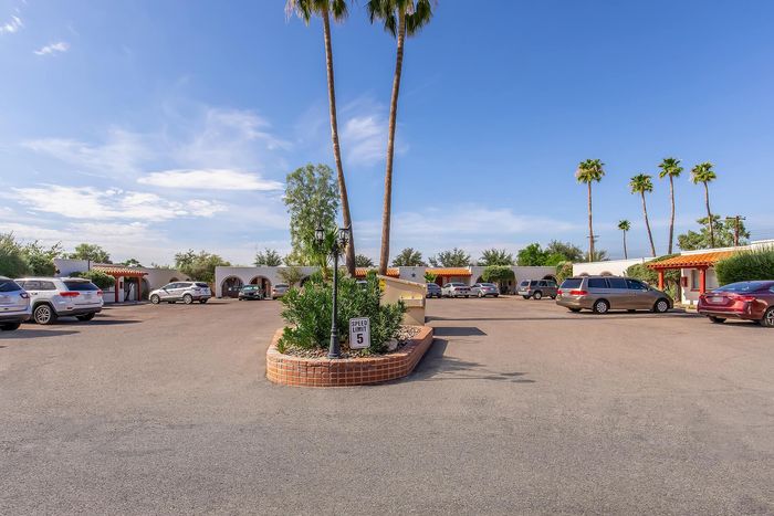 Inviting apartment complex with charming Spanish-style architecture, lush palm trees, and ample parking space under a clear blue sky.