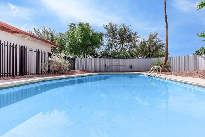 Inviting outdoor pool area surrounded by lush greenery and modern fencing under a clear blue sky.