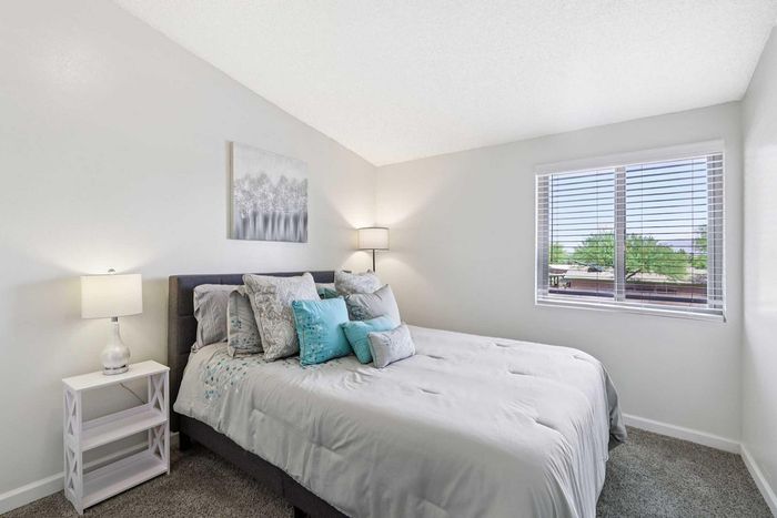 Bright and airy bedroom with soft neutral tones, plush bedding, stylish wall art, and large window offering a scenic view.