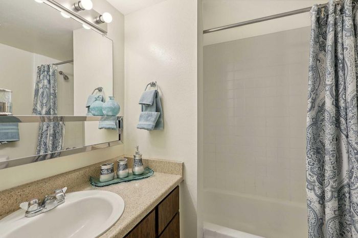 Chic bathroom with elegant blue accents, featuring a large mirror, granite countertop, and patterned shower curtain.