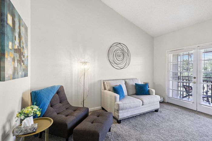 Bright living room with modern decor, featuring a plush gray sofa, elegant armchairs, and a glass door leading to a sunlit patio, creating a welcoming and cozy atmosphere.