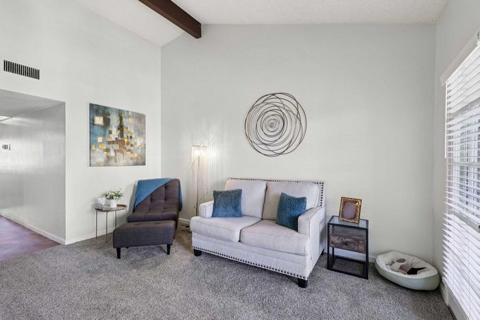 Elegant and cozy living room featuring a plush gray chair, stylish white sofa with blue accent pillows, modern artwork, and natural light streaming through large windows.