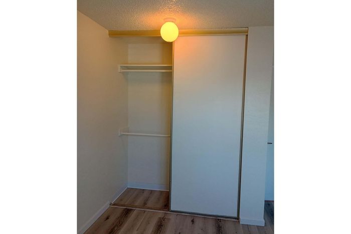 Modern closet with sliding doors, illuminated by a warm ceiling light, featuring sleek shelving and polished wooden flooring.