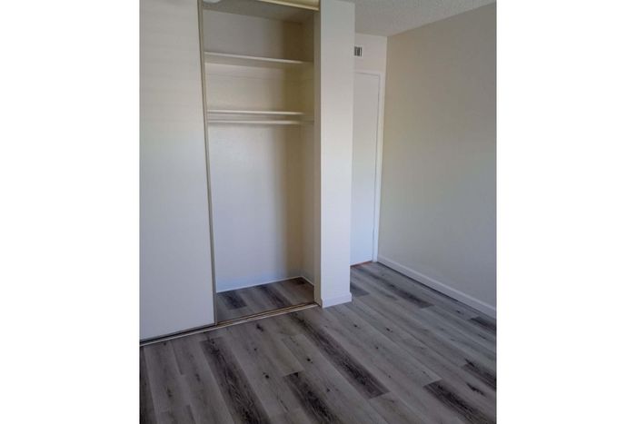 Modern bedroom with sleek laminate flooring and a spacious open closet, offering ample storage in a fresh and inviting space.
