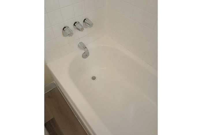 Pristine white bathtub with modern chrome fixtures and tiled surround, exuding a sleek and relaxing bathroom ambiance.