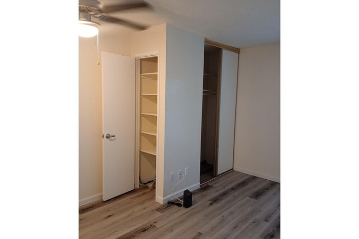 Modern bedroom featuring sleek laminate flooring, ample closet space with mirrored sliding doors, and built-in shelving for optimal storage solutions.