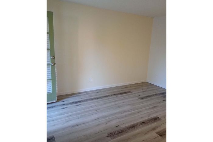 Inviting room with fresh paint, sleek light wood flooring, and an elegant green door, perfect for customization.