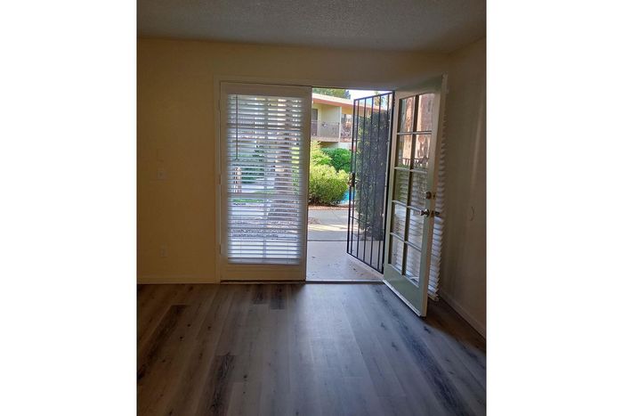 Bright living area with elegant hardwood floors, featuring glass doors opening to a lush garden view.