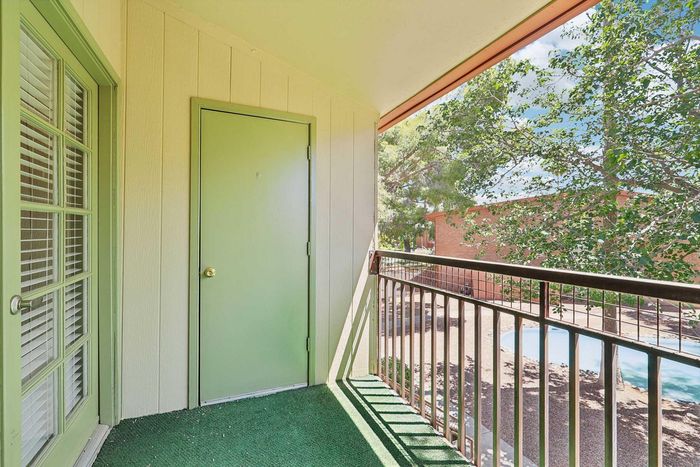 Charming apartment balcony with lush green carpet, overlooking a serene courtyard with trees and a glimpse of a pool, perfect for relaxing outdoors.