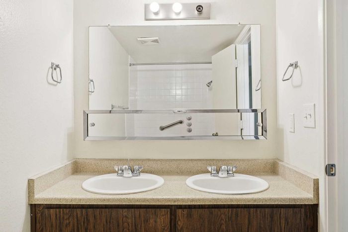 Elegant bathroom showcasing a dual-sink vanity with sleek fixtures and a large mirror in a modern apartment setting.