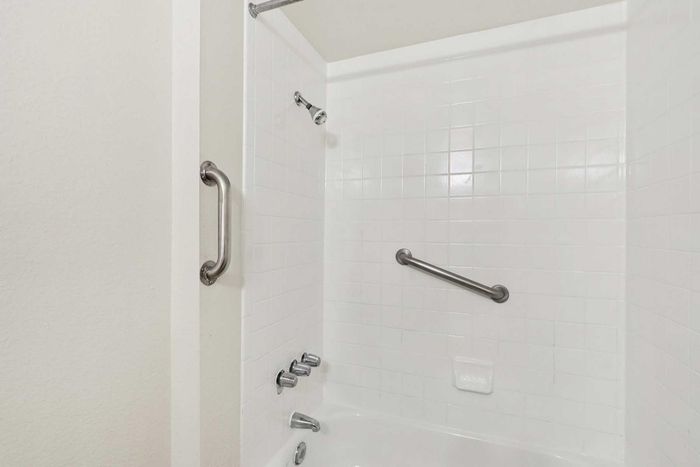 Modern bathroom with sleek white tiles, chrome fixtures, and a built-in safety grab bar for comfort and security.