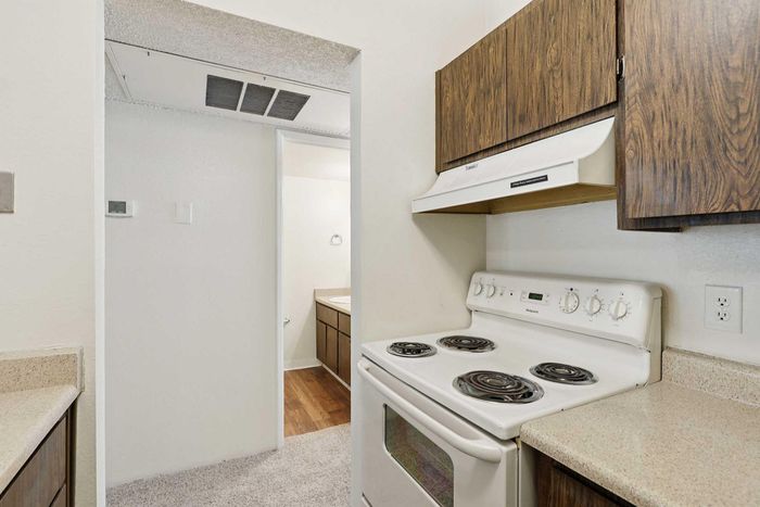 Cozy kitchen with classic electric stove, elegant wooden cabinets, and sleek countertops leading to a bright bathroom.