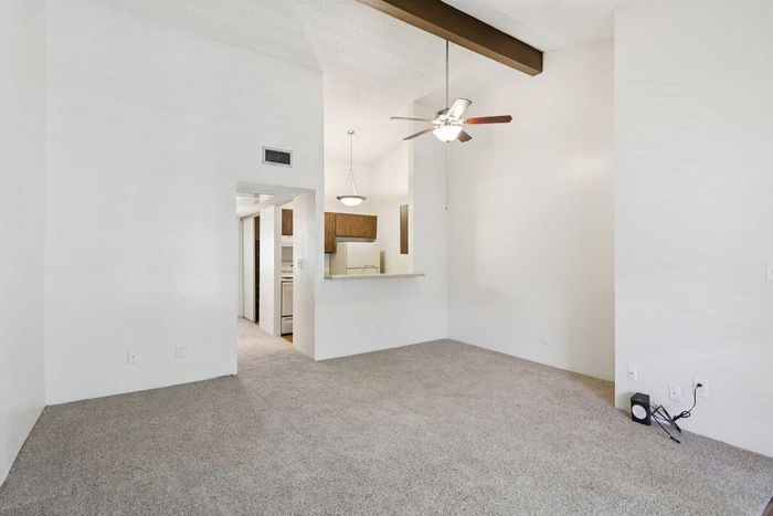 Bright, spacious living area with vaulted ceiling and cozy carpet, adjacent to a modern kitchen. Ideal for creating a warm home atmosphere.