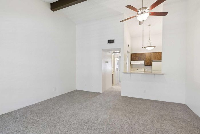Inviting living space featuring an elegant ceiling fan, plush carpet, and seamless access to a charming kitchen with wooden cabinets.