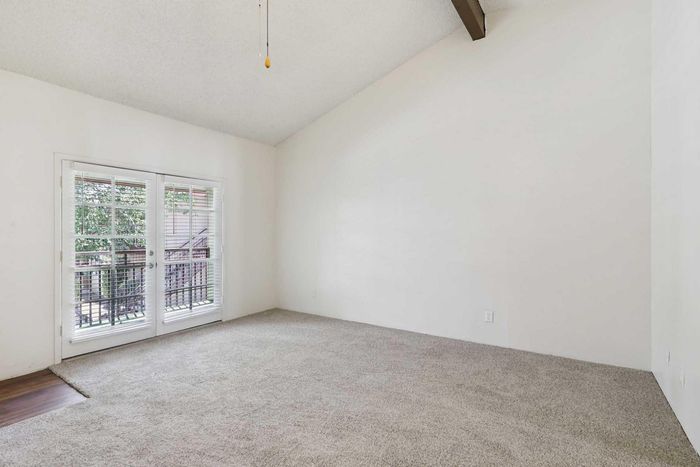 Bright and spacious room with plush carpeting, high ceiling, and expansive windows opening to a serene outdoor view.
