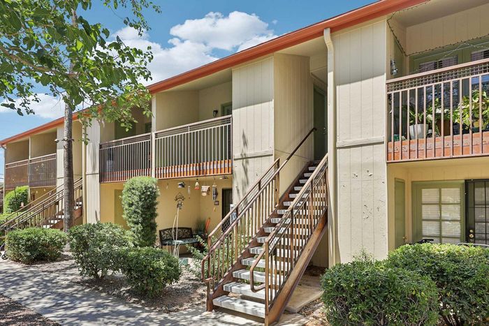 Charming multi-unit apartment building with lush greenery and inviting balconies, offering a welcoming and serene living environment.