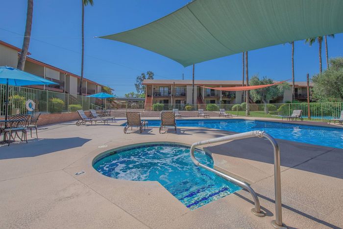 Inviting apartment complex pool area with sun loungers, shaded seating, and lush surroundings for a perfect relaxation spot.