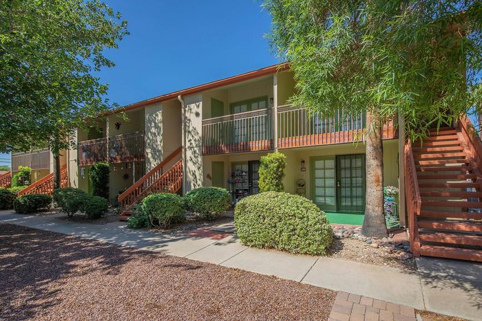 Charming apartment complex with lush landscaping, cozy private patios, and vibrant greenery under a clear blue sky.