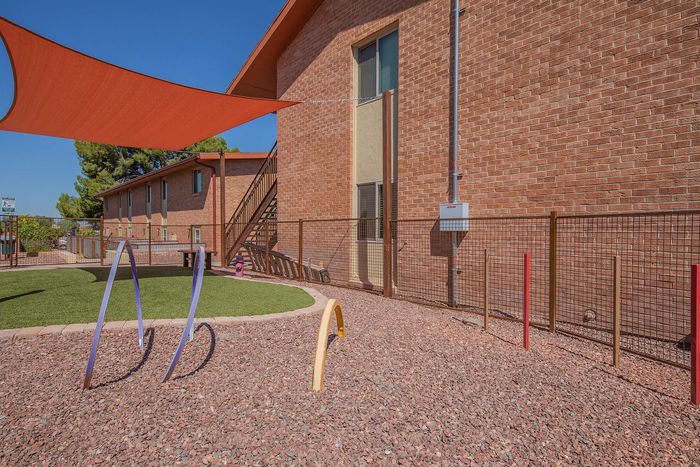 Charming outdoor play area with vibrant climbing bars, framed by modern brick apartments under a clear blue sky.