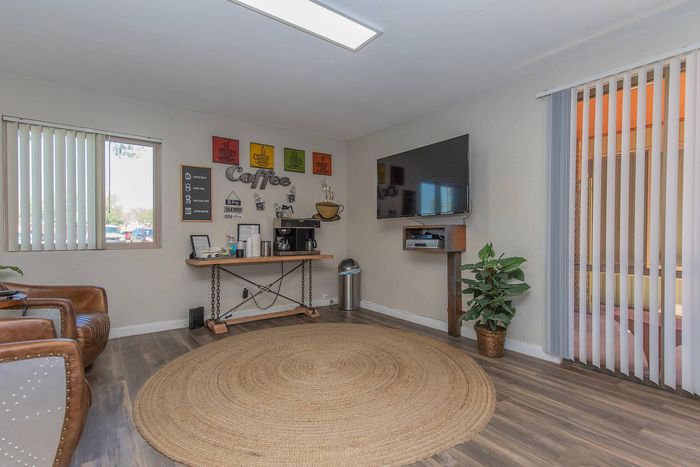 Cozy living area with stylish coffee nook, leather chairs, large wall-mounted TV, and natural light through vertical blinds.
