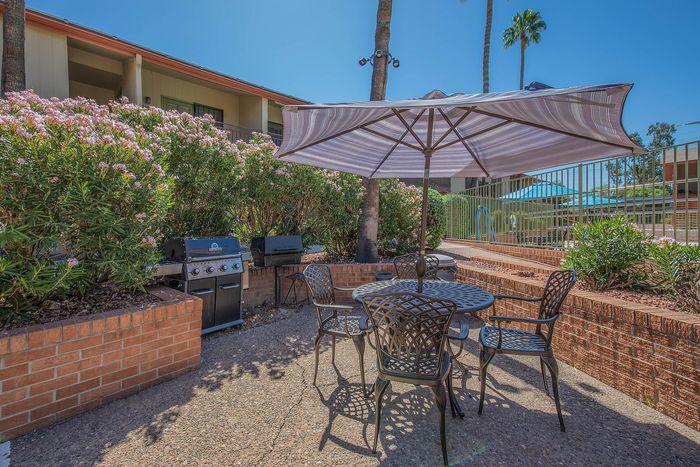 Charming outdoor patio with elegant metal furniture and a large striped umbrella, perfect for hosting barbecues next to lush flowering shrubs.