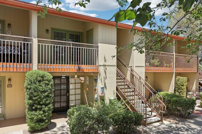 Charming two-story apartment exterior with lush greenery, cozy balcony, and inviting entrance, offering a serene living environment.