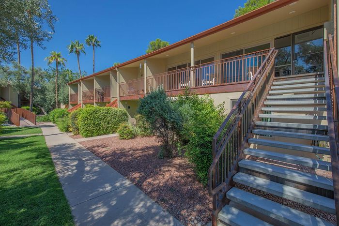 Charming apartment complex with spacious balconies, surrounded by lush greenery and palm trees under a clear blue sky.